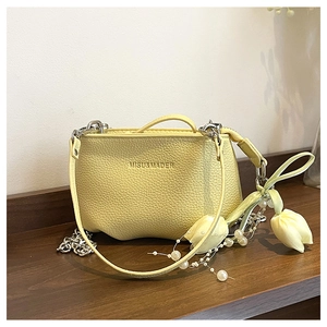 Détail d'un sac seau jaune vif en cuir grainé avec chaîne argentée et charm perle et fleur