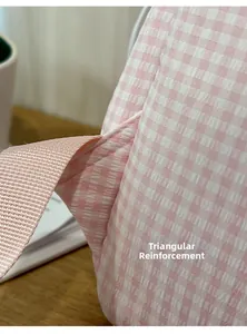 Détail du renfort triangulaire des bretelles sur un sac à dos à carreaux rose et blanc