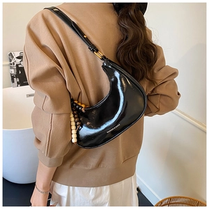 Detail of glossy black patent leather crescent bag with decorative wooden beads