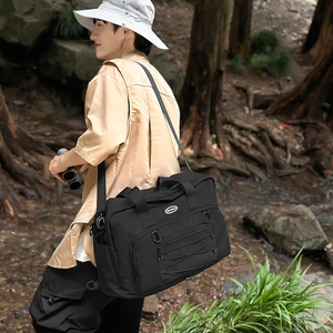 Close-up of black multi-pocket canvas bag with bungee cord detail in forest setting