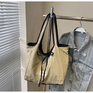Close-up of khaki tote bag with navy trim, bow detail and minimalist fabric label