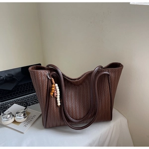 Detail of dark brown woven tote bag featuring a V-shaped texture and wooden beaded charm