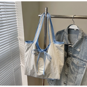Detail of cream and light blue tote bag with a bow tie closure on a metal hanger