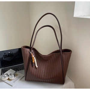 Detail view of large brown woven tote bag with beads on a minimalist desk setup