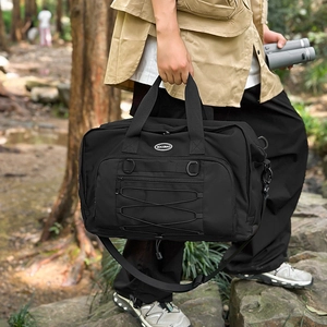 Outdoor view of a black tactical travel bag with front elastic cords and D-ring buckles