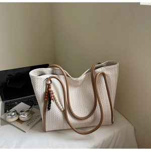 Detail of beige woven tote bag with V-shaped texture, leather handles, and beaded charm