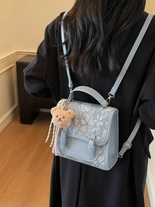 Fashionable light blue floral backpack with brown teddy bear charm worn by a person