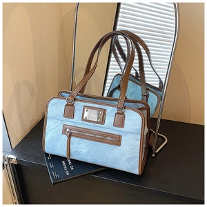 Detail view of washed denim tote bag with brown leather trim and metal logo plate