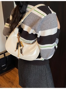 Chic beige crescent shoulder bag with beaded charm accessory shown on a female model