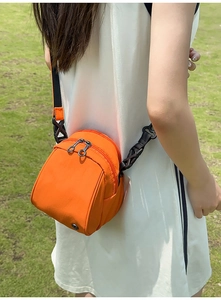 Detalle de bolso bandolera de nailon naranja brillante con doble cremallera sobre vestido