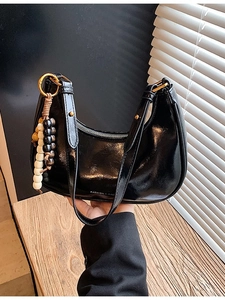Chic black glossy crescent shoulder bag with beaded charm and gold-tone hardware