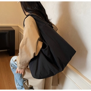 Detail of a black minimalist large canvas tote bag with long strap on a beige trench coat