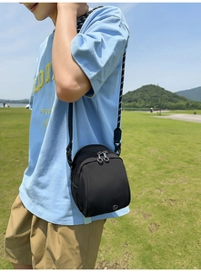 Detalle del bolso bandolera de nailon negro con doble cremallera y correa de lunares