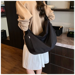 Detail of minimalist black crescent bag showing wide shoulder strap and fabric texture