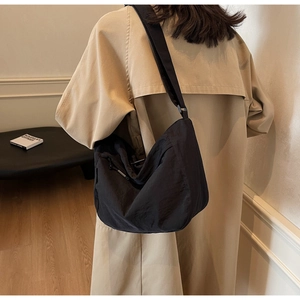 Close-up of black pleated dumpling bag with wide adjustable strap worn on khaki trench coat