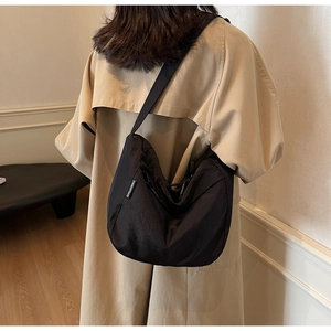Detail of black pleated hobo bag with wide strap and QIUHANMAO label worn by model