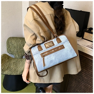 Close-up of light blue textured tote bag with brown leather trim and metal logo plate