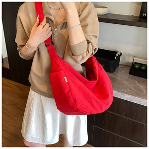 Detail of red crescent-shaped nylon crossbody bag with textured fabric and woven label