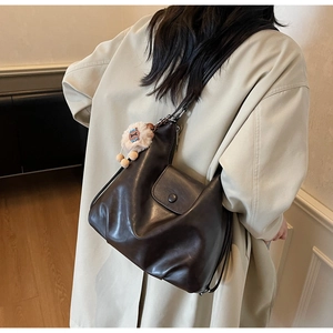 Dettaglio di una borsa tote in pelle marrone con ciondolo peluche su un trench beige