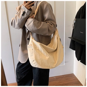 Detail of a large beige crossbody dumpling bag showing a wide strap and pleated design