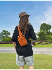 Foto de estilo de vida de un bolso bandolera de lona naranja en un modelo en un parque