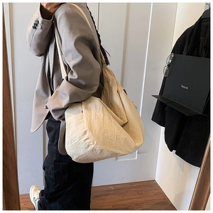 Detailed view of a beige slouchy nylon shoulder bag with spacious interior and side label