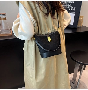 Gros plan d'un sac seau matelassé noir avec fermoir doré porté sur un manteau beige