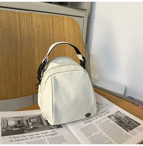 Detalle de bolso bandolera de nailon blanco con asa superior y logotipo metálico