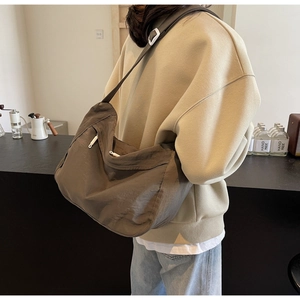 Brown nylon crossbody bag shown on model in a cozy coffee shop setting with a wide strap