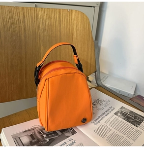 Detalle de un bolso bandolera de nailon naranja brillante con asa de hebilla negra