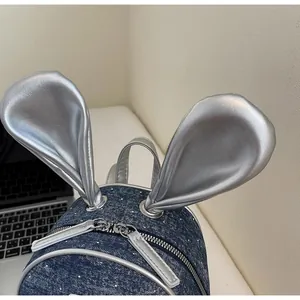 Detail of denim backpack with silver rabbit ears and white polka dots on desk