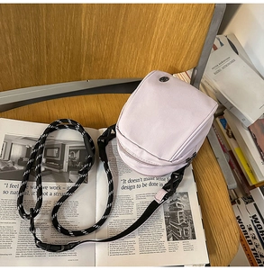 Detalle de bolso bandolera de nailon lila con correa tejida sobre revistas