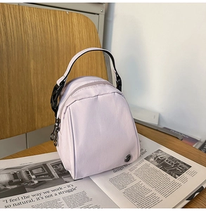 Primer plano de un mini bolso de nailon lila sobre una revista con logo metálico