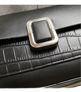 Detail of black crossbody bag featuring mixed crocodile texture and silver metal clasp