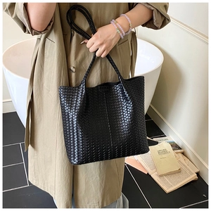 Detail view of black woven leather tote bag featuring modern geometric texture and handles