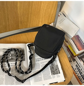 Detalle de un bolso bandolera de nailon negro con cremalleras y correa de hombro tejida