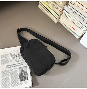 Detalle de bolso bandolera de nailon negro sobre fondo de libros y revistas minimalista