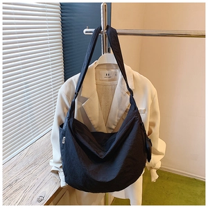 Detail of black nylon crescent bag with wide strap on white blazer, minimalist style