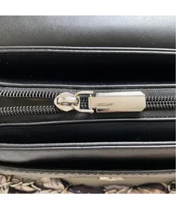 Close-up of smooth silver metal zipper puller on minimalist black leather crossbody bag