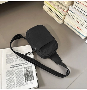 Vista de detalle de un bolso bandolera de nailon negro con bolsillos en un escritorio sobrio
