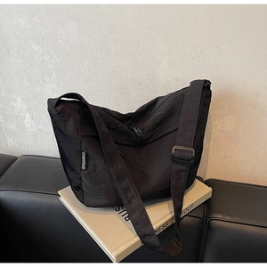 Detail showing the adjustable wide strap and white brand label on a black pleated crossbody bag