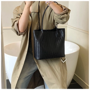 Detail of a black woven leather tote bag texture with minimalist woven shoulder straps