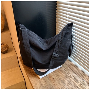 Close-up of a large black crescent crossbody bag with nylon texture on a wooden desk
