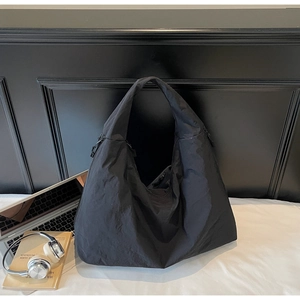 Detail showing the textured nylon surface of a black tote bag with laptop and headphones