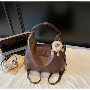 Dettaglio di una borsa Hobo marrone con ciondolo in peluche su letto con laptop