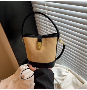 Détail d'un sac seau beige matelassé avec finitions en cuir noir et fermoir doré rotatif
