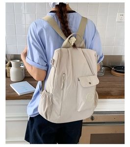 Rear view of a large capacity cream travel backpack worn by a model in a kitchen