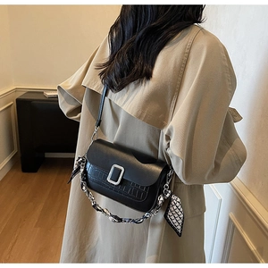 Detail of black faux leather crossbody bag with crocodile pattern and silk scarf chain