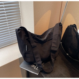 Detail of nylon crossbody bag featuring woven brand label and adjustable strap