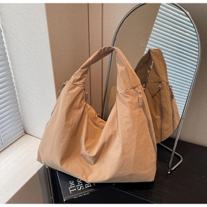 Detail of khaki hobo bag with unique side zippers and textured nylon fabric on books